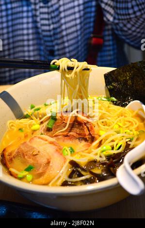 Essstäbchen nehmen japanische Tonkotsu-Ramen mit Algen, Schweinefleisch (Tonkotsu), Bohnensprossen und Frühlingszwiebeln in einer Schüssel auf. Stockfoto