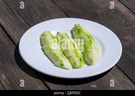 Selektive Fokusansicht der Platte mit in Scheiben geschnittenen Gurken auf einem Holztisch. Stockfoto