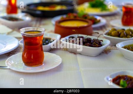 Das Frühstück steht mit einem weißen Bodentuch auf dem Tisch; Tee-Olivenplatten, Grüns-, Käse- und Joghurtplatten. Stockfoto