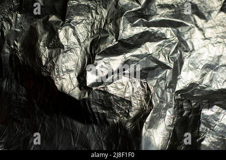 Folienstruktur. Zerknittert gerippte Folie. Unebene Hintergrundoberfläche reflektiert Licht. Stockfoto