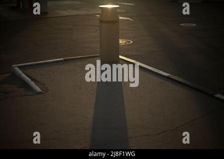 Urne auf dem Parkplatz. Ort, um Müll auf der Straße zu sammeln. Schatten von Müll auf Asphalt. Parkdetails. Stockfoto