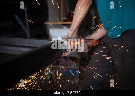 Arbeiten Sie mit einem Mahlwerk für Metall. Funken durch Metallreibung. Ein Arbeiter mahlen ein Teil. Stahlbearbeitung mit einem Elektrowerkzeug. Erstellung der Struktur Stockfoto