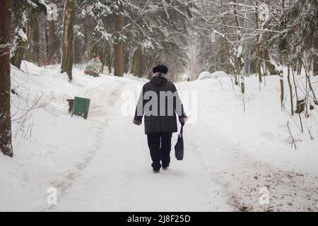 Älterer Mann läuft im Winter durch den Park. Menschen in der Stadt. Aufnahmen von hinten. Rentner in Russland. Es ist ein kalter Tag. Stockfoto