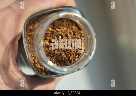 Instant-Kaffee im Glas. Kaffee in der Hand. Zutat für Getränke. Hand hält Glasbehälter mit gefriergetrocknetem Getränk aus Kaffeebohnen. Stockfoto