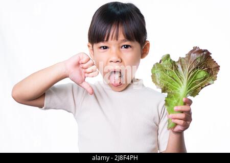 Kinder essen nicht gerne Gemüse. Kleines Mädchen, das es hasst, grünen Salat zu essen. Stockfoto