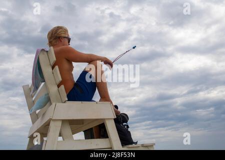 Strandschwimmer auf einem Hochsessel mit Blick auf das Meer und mit einer Pfeife auf einem Trageband Stockfoto