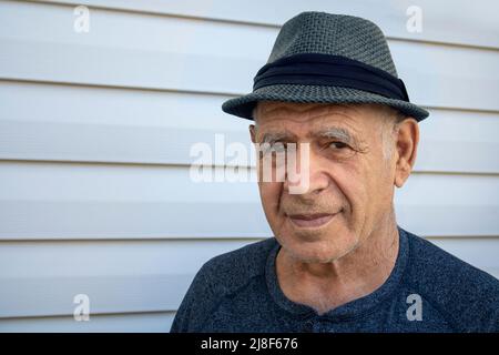 kaukasischer älterer Erwachsener mit einem Fedora-Hut vor einer weißen Hauswand Stockfoto