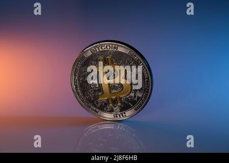 Bitcoin BTC Kryptowährung physische Münze auf reflektierender Oberfläche platziert und mit orangefarbenen und blauen Lichtern beleuchtet. Makroaufnahme. Selektiver Fokus. Stockfoto