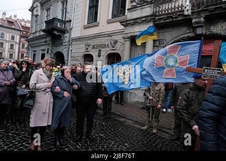 Mitglieder des Kultschizki-Bataillons der ukrainischen Nationalgarde tragen den Sarg von Iwan Wolodymyrowytsch Datsko, der in der Region Donezk getötet wurde, zu einem wartenden Fahrzeug, während Angehörige seiner Familie und Freunde auf ihn blicken. Stockfoto