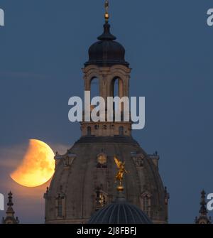 Dresden, Deutschland. 16.. Mai 2022. Der Mond geht morgens bei einer partiellen Mondfinsternis hinter der Frauenkirche und der Kuppel der Kunstakedmie mit dem Engel 'Fama' unter. Zuschauer können heute Morgen eine totale Mondfinsternis beobachten, aber nicht überall. An einigen Stellen wird der Mond bereits hinter dem Horizont im Südwesten verschwinden, bevor er vollständig in den Schatten der Erde taucht. So konnten Beobachter teilweise nur eine partielle Mondfinsternis beobachten. Kredit: Robert Michael/dpa/Alamy Live Nachrichten Stockfoto