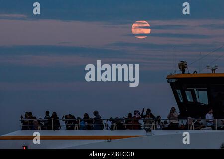 Istanbul, Türkei. 15.. Mai 2022. Ein Supermond am Himmel mit Passagieren auf der Terrasse der City Lines Fähre. Der Supermond, der beim Sonnenuntergang in Istanbul am Abend auftauchte, wurde durch die Wolken gesehen. (Foto von Onur Dogman/SOPA Images/Sipa USA) Quelle: SIPA USA/Alamy Live News Stockfoto