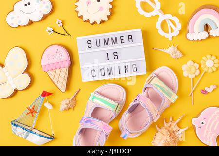 Der Sommer kommt. Motivationszitat auf Leuchtkasten und niedlichen Sommer-Symbolen auf gelbem Hintergrund. Draufsicht, Flat Lay. Kreative inspirierende Sommerkonz Stockfoto