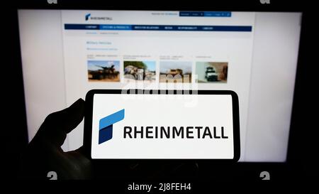 Person, die Mobiltelefon mit Logo der Rheinmetall AG auf dem Bildschirm vor der Business-Webseite hält. Konzentrieren Sie sich auf die Telefonanzeige. Stockfoto