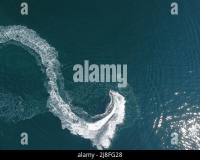 Luftaufnahme von oben nach unten von Wasserschaumspuren mit schönem tiefblauen Schatten des Ozeans. Schöne weiße Spur auf der ruhigen Meeresoberfläche hinter einem kleinen mächtigen Stockfoto