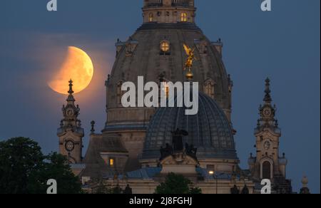 Dresden, Deutschland. 16.. Mai 2022. Der Mond geht morgens bei einer partiellen Mondfinsternis hinter der Frauenkirche und der Kuppel der Kunstakedmie mit dem Engel 'Fama' unter. Zuschauer können heute Morgen eine totale Mondfinsternis beobachten, aber nicht überall. An einigen Stellen wird der Mond bereits hinter dem Horizont im Südwesten verschwinden, bevor er vollständig in den Schatten der Erde taucht. So konnten Beobachter teilweise nur eine partielle Mondfinsternis beobachten. Kredit: Robert Michael/dpa/Alamy Live Nachrichten Stockfoto
