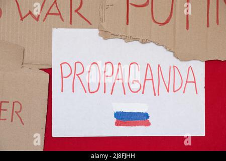 Papierschilder mit Slogans stoppen Krieg, Propaganda und die russische Flagge auf rotem Hintergrund, eine Protestaktion 2022 Stockfoto