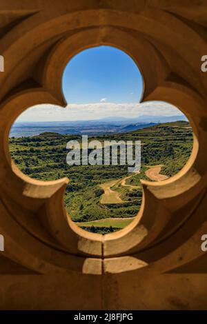 Atemberaubende Aussicht auf das terrassenförmige Tal durch einen reich verzierten Quatrefoil oculus auf die gotische Arkade der Festungskirche Iglesia de Santa Maria in Ujue, Spanien Stockfoto