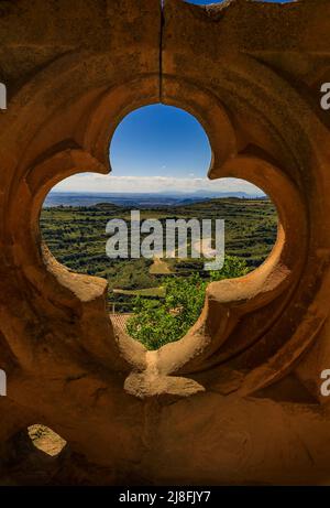 Atemberaubende Aussicht auf das terrassenförmige Tal durch einen reich verzierten Quatrefoil oculus auf die gotische Arkade der Festungskirche Iglesia de Santa Maria in Ujue, Spanien Stockfoto