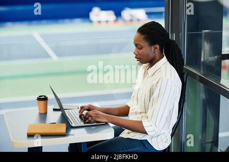 Seitenansicht Porträt einer jungen schwarzen Frau, die einen Laptop benutzt, während sie im Sporttrainingszentrum arbeitet Stockfoto