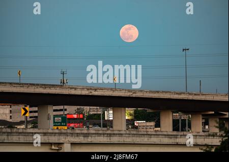 Austin, Texas, USA. 15. Mai 2022. Der Vollmond steigt über der Stadt Austin auf, die 183 North Overpass ist im Vordergrund zu sehen. Dieses erste rote Zeichen stammt vom Sonnenuntergang, aber der Mond am Sonntagabend, dem 15.. Mai, wird als Super Flower Blood Moon bezeichnet. Später an diesem Abend wird es eine Sonnenfinsternis geben, die dem Mond eine rote Farbe verleiht. Er wird Blumenmond genannt, weil im Mai viele Blumen wachsen. Kredit: Sidney Bruere/Alamy Live Nachrichten Stockfoto