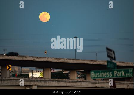 Austin, Texas, USA. 15. Mai 2022. Der Vollmond steigt über der Stadt Austin auf, die 183 North Overpass ist im Vordergrund zu sehen. Dieses erste rote Zeichen stammt vom Sonnenuntergang, aber der Mond am Sonntagabend, dem 15.. Mai, wird als Super Flower Blood Moon bezeichnet. Später an diesem Abend wird es eine Sonnenfinsternis geben, die dem Mond eine rote Farbe verleiht. Er wird Blumenmond genannt, weil im Mai viele Blumen wachsen. Kredit: Sidney Bruere/Alamy Live Nachrichten Stockfoto