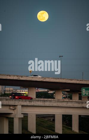 Austin, Texas, USA. 15. Mai 2022. Der Vollmond steigt über der Stadt Austin auf, die 183 North Overpass ist im Vordergrund zu sehen. Dieses erste rote Zeichen stammt vom Sonnenuntergang, aber der Mond am Sonntagabend, dem 15.. Mai, wird als Super Flower Blood Moon bezeichnet. Später an diesem Abend wird es eine Sonnenfinsternis geben, die dem Mond eine rote Farbe verleiht. Er wird Blumenmond genannt, weil im Mai viele Blumen wachsen. Kredit: Sidney Bruere/Alamy Live Nachrichten Stockfoto