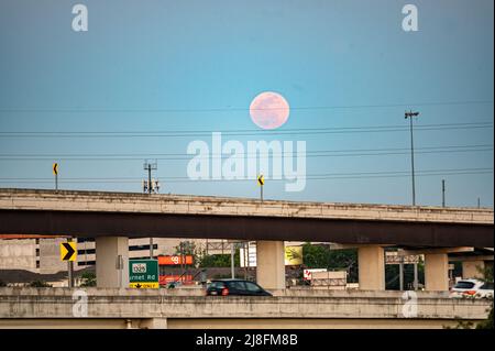 Austin, Texas, USA. 15. Mai 2022. Der Vollmond steigt über der Stadt Austin auf, die 183 North Overpass ist im Vordergrund zu sehen. Dieses erste rote Zeichen stammt vom Sonnenuntergang, aber der Mond am Sonntagabend, dem 15.. Mai, wird als Super Flower Blood Moon bezeichnet. Später an diesem Abend wird es eine Sonnenfinsternis geben, die dem Mond eine rote Farbe verleiht. Er wird Blumenmond genannt, weil im Mai viele Blumen wachsen. Kredit: Sidney Bruere/Alamy Live Nachrichten Stockfoto