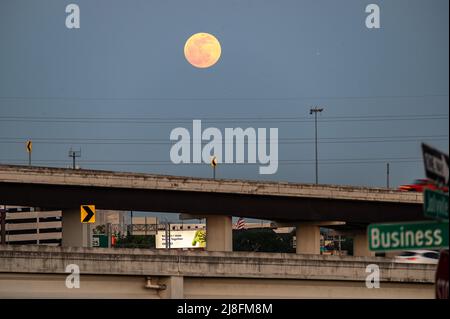 Austin, Texas, USA. 15. Mai 2022. Der Vollmond steigt über der Stadt Austin auf, die 183 North Overpass ist im Vordergrund zu sehen. Dieses erste rote Zeichen stammt vom Sonnenuntergang, aber der Mond am Sonntagabend, dem 15.. Mai, wird als Super Flower Blood Moon bezeichnet. Später an diesem Abend wird es eine Sonnenfinsternis geben, die dem Mond eine rote Farbe verleiht. Er wird Blumenmond genannt, weil im Mai viele Blumen wachsen. Kredit: Sidney Bruere/Alamy Live Nachrichten Stockfoto