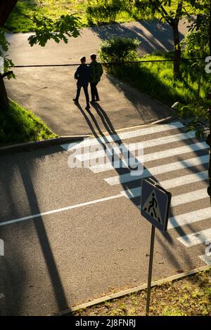 Ein Paar läuft über den Fußgängerübergang an der Kreuzung der Stadt. Fußgängersicherheit. Silhouetten von Menschen, die einen Fußgängerüberweg überqueren. Fußgänger überqueren Stockfoto