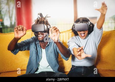 Ein paar glückliche Freunde genießen ein virtuelles 3D-Spiel mit Virtual-Reality-Brille auf dem Sofa sitzen innen - Tech-und People Lifestyle-Konzept Stockfoto