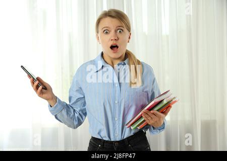 Junge attraktive Frau mit Copybooks und Telefon in Panik Stockfoto
