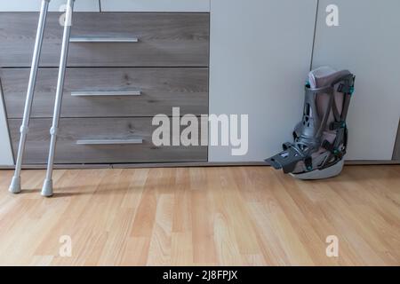 Europäischer Mann nach Achillessehnenriss Operation ist wieder zu Hause mit Moon Boot speziellen physiotherapeutischen Schuh und Krücken für die Erholung zu Hause gegen Stockfoto