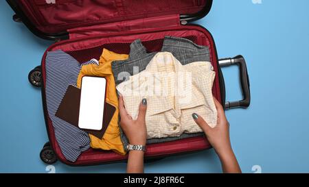 Frau, die Kleidung in den Koffer packt. Vorbereitung auf die Sommerferien Stockfoto