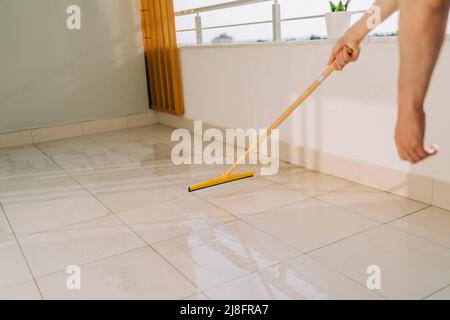 Mann, der mit dem Mopp den Boden abwischt. Der Hausmeister wasch die schmutzigen Böden. Mann, der an einem sonnigen Tag den Balkon wischt. Person, die Hausaufgaben erledigt. Junger Mensch, der verwendet Stockfoto