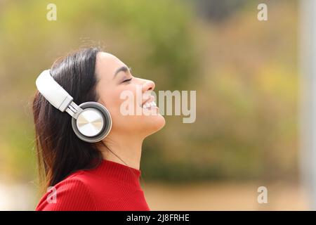 Seitenansicht Porträt einer glücklichen Frau, die in einem Park mit kabellosen Kopfhörern Musik hört Stockfoto