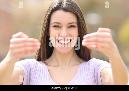 Vorderansicht Porträt eines glücklichen Teenagers, der sagt, dass er mit beiden Händen in einem Park zur Kamera kommt Stockfoto