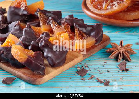 Kandierte orangefarbene Scheiben, die mit Schokolade auf einem Holzhintergrund bedeckt sind. Stockfoto