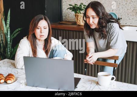 Erwachsene lächelnd Brünette mittleren Alters Frauen Schwestern Freunde beim Frühstück und mit Laptop in der Küche zu Hause Stockfoto