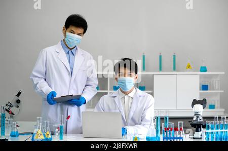 Zwei Wissenschaftler mit Gesichtsmaske und Kittel arbeiten im Labor. Omicron Strain Testing Process, Coronavirus Disease 2019. Stockfoto