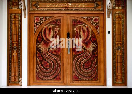 Geschnitzte Holztür Detail mit Hahn Huhn Figuren mit beeindruckenden Gefieder Thailand Südostasien Stockfoto