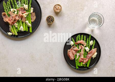 Grüner Spargel mit Mozzarella-Käse und Prosciutto-Schinken. Köstliche Gerichte der Saison. Blick von oben auf zwei Teller, Keto Diätmenü Mittag- oder Abendessen. Stockfoto