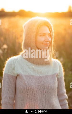 Portrait of Young Pretty Caucasian Happy Girl Woman in Woolen Jacket Bluse und Brown gestrickte Haube posiert im frühen Frühlingswald in Sunny Day. Viel Spaß Stockfoto