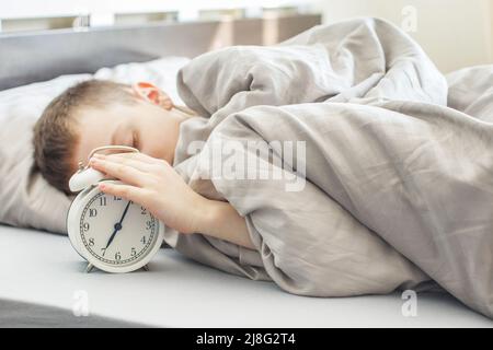 Junge auf dem Bett liegen und stoppen Wecker am Morgen. kinder Hand griff nach dem Wecker, um ihn auszuschalten. Stockfoto