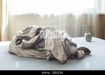 Zerknittert leeres Bett in einem Zimmer auf einem Fensterhintergrund. Wochenende morgens, Einsamkeit. Chaotische Decke im Schlafzimmer nach dem Aufwachen Stockfoto