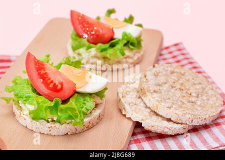 Reiskuchen-Sandwiches mit Tomaten, Salat und Ei auf Holzbrett. Einfaches Frühstück. Diät-Essen. Schnelle und gesunde Sandwiches. Knäckebrot mit leckerer Füllung. Gesunder Ernährungs-Snack Stockfoto