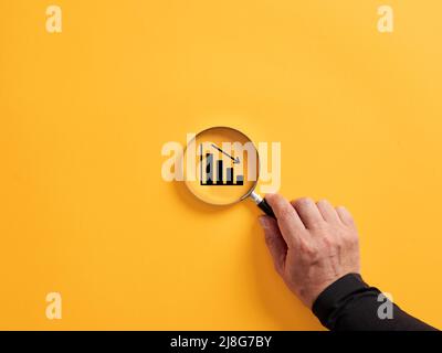 Hand mit einer Lupe über dem absteigenden oder absteigenden Graphen halten. Konzept der Wirtschaftskrise und der finanziellen Rezession. Stockfoto