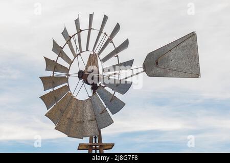 Nahaufnahme einer alten Metallmühle zur Wassergewinnung mit teilweise bewölktem Himmel im Hintergrund. Es hat viele Klingen und einen Metallschwanz, um seine Richtung zu variieren Stockfoto