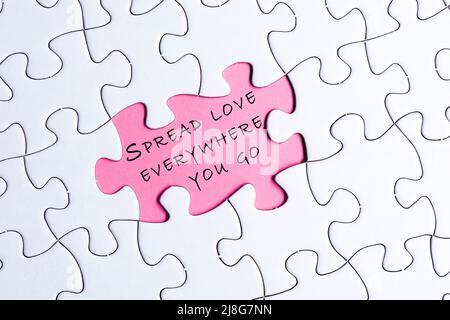 Weißes Puzzle mit motivierendem und inspirierendem Zitat auf violettem Hintergrund – verbreiten Sie Liebe überall. Stockfoto