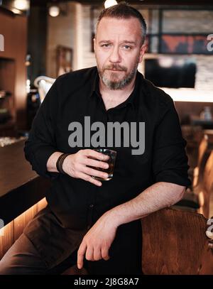 Porträt eines hübschen reifen Mannes, der ein Glas ordentlichen Whiskys in der Bar oder im Pub hält. Stockfoto