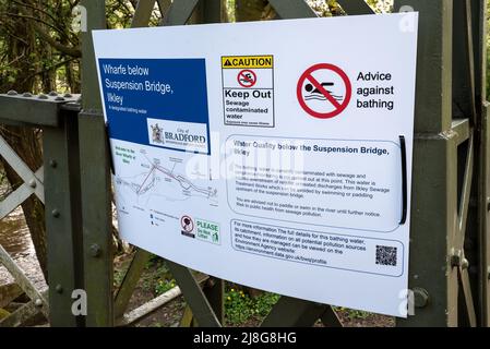 Großes Warnschild für Abwasserkontamination am Fluss Wharfe in Ilkley, Yorkshire, Großbritannien. Warnung zum Abhalten, Abwasser kontaminiertes Wasser. Regelmäßige, unbehandelte Rohtabwässer, die aus ca. 250m Abwasserwerken stromaufwärts in ausgewiesene Badegewässer eingeleitet werden. Der Vorsitzende des Regierungsausschusses, Philip Dunne, sagte, dass im Jahr 2021 über 370.000 Mal Abwasser in unsere Wasserstraßen geschüttet wurde, das sei einfach nicht hinnehmbar. Kredit: Stephen Bell/Alamy Stockfoto